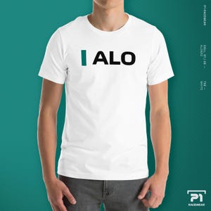 K&ouml;nnte beinhalten: Wei&szlig;es T-Shirt mit dem Text "I ALO" in Schwarz und Blaugr&uuml;n. Das Shirt ist Teil der P1 Racewear-Kollektion mit dem Alonso-Design. Das T-Shirt ist wei&szlig;.