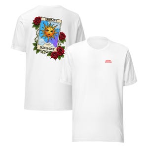 May include: White t-shirt featuring a tarot card design on the back with a grumpy sun illustration, surrounded by roses and thorns. The text "GRUMPY SUNSHINE" is displayed. The front of the shirt has the text "GRUMPY SUNSHINE" in red.