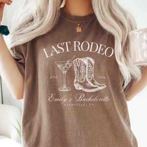May include: Brown t-shirt with white text that reads "Last Rodeo June 2024 Emily's Bachelorette Nashville, TN". The shirt also features a white illustration of a martini glass and cowboy boots.