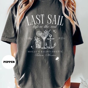 May include: A gray t-shirt with white text that reads "Last Sail Before the Veil" with a cocktail and anchor graphic. The text also includes "Aug 2021" and "Molly's Bachelorette Tulum, Mexico".