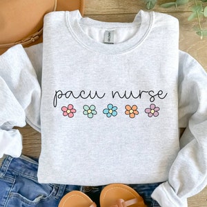 May include: A gray sweatshirt with the text "pacu nurse" in black script. Five colorful flowers are arranged in a row below the text.