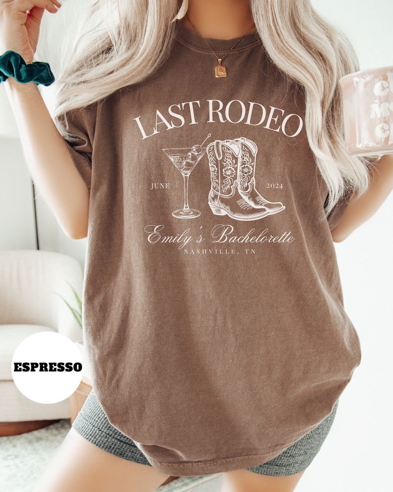May include: Brown t-shirt with white text that reads "Last Rodeo June 2024 Emily's Bachelorette Nashville, TN". The shirt also features a white illustration of a martini glass and cowboy boots.