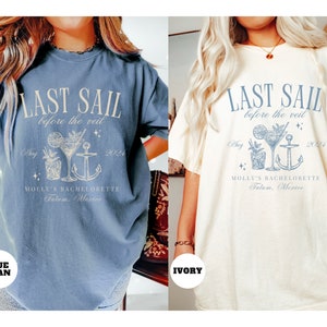 May include: Two t-shirts with a graphic design of a cocktail, anchor, and the text "Last Sail Before the Veil" in a light blue color. The text "Molly's Bachelorette Tulum, Mexico" and "Aug 2024" are also included in the design. The t-shirt on the left is blue jean and the t-shirt on the right is ivory.