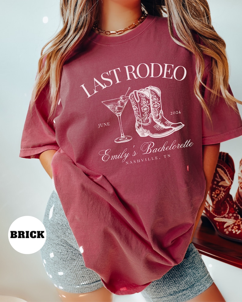 May include: A maroon t-shirt with the text "Last Rodeo" in white, featuring a pair of cowboy boots and a martini glass. The text "Emily's Bachelorette" is also in white, along with the date "June 2024" and the location "Nashville, TN".