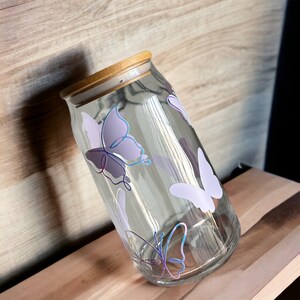 May include: A clear glass jar with a wooden lid and a butterfly design. The butterflies are purple, blue, and white.