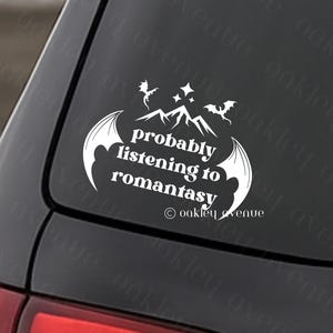 Può includere: Adesivo in vinile bianco con la scritta "probably listening to romantasy" in un font stilizzato, con grafiche di montagne e ali di pipistrello. Applicato sul finestrino di un'auto.