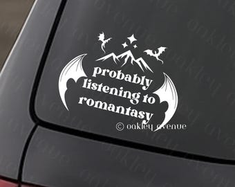 May include: White vinyl decal with the text "probably listening to romantasy" in a stylized font, featuring mountain and bat wing graphics. The decal is affixed to a car window.