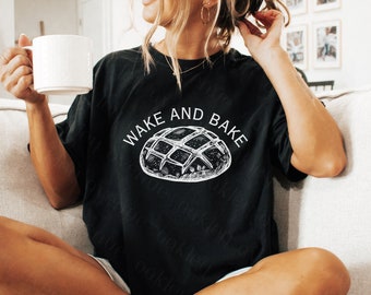 Könnte beinhalten: Ein schwarzes T-Shirt mit dem Text "Wake and Bake" und einer weißen Illustration eines Laibes Brot.