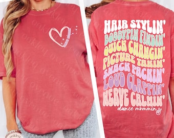 Op de afbeelding: Rood T-shirt met een wit hart en de tekst "Dance Mommin'" op de rug. De tekst is in een regenboogkleurenschema en bevat de woorden "Hair Stylin', Bobbypin Findin', Quick Changin', Picture Takin', Snack Packin', Loud Clappin', Nerve Calmin'."
