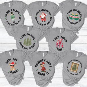 May include: A collection of gray t-shirts with various Christmas-themed graphics and text. Designs include a nutcracker, Santa Claus, Christmas ornaments, Christmas trees, elves, a reindeer, and an elf. Each shirt has a unique phrase.