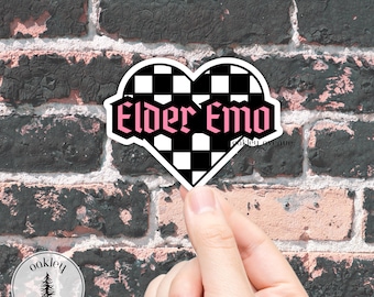 Puede incluir: Una pegatina en forma de corazón con un patrón de cuadros blancos y negros y las palabras "Elder Emo" en rosa. La pegatina se sostiene contra un fondo de pared de ladrillo.