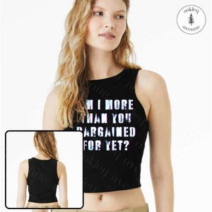 May include: Black crop top with the text "AM I MORE THAN YOU BARGAINED FOR YET?" in white and blue. The top is sleeveless and has a round neckline. The image also includes a small inset image of the back of the top.