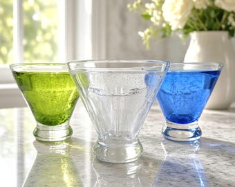 May include: Three glass bowls with a wide rim and a thick base. One bowl is lime green, one is clear, and one is cobalt blue. Each bowl features a textured surface with small air bubbles embedded within the glass, creating a distinct appearance.