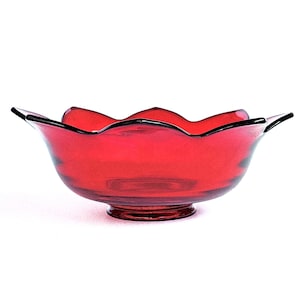 May include: A ruby red glass bowl with a scalloped rim and a circular base. The bowl's edges are outlined in black, and the overall shape resembles a flower. The bowl is transparent, allowing light to pass through.