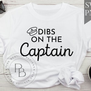 Puede incluir: Camiseta blanca con texto negro que dice "Dibs on the Captain" y una pequeña imagen de un sombrero de capitán con un ancla.