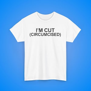 May include: White crew neck t-shirt featuring the black text "I'M CUT (CIRCUMCISED)". The shirt is displayed on a blue background. The text is centered on the front of the shirt, making a bold statement.