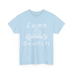 May include: Light blue t-shirt with a white graphic. The graphic features the words "Sumo Deadlift" with an illustration of a sumo wrestler lifting a barbell. The shirt is made of a soft material and has short sleeves.