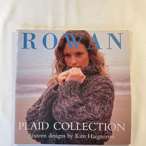 May include: A book titled "Rowan Plaid Collection" with a woman wearing a brown and grey knitted sweater on the cover. The text "Sixteen designs by Kim Hargreaves" is printed below the title.