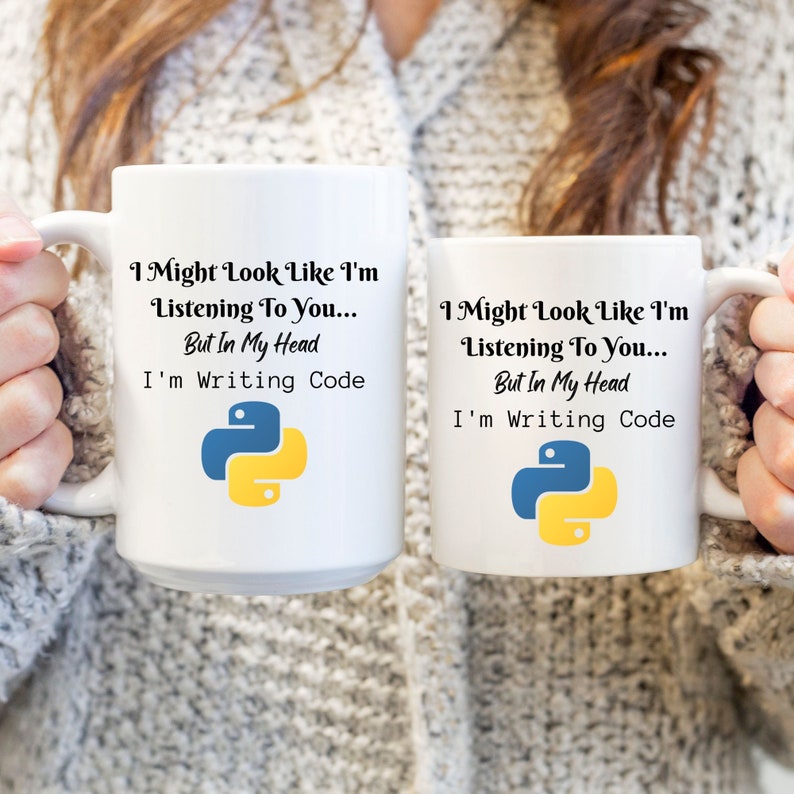 K&ouml;nnte beinhalten: Zwei wei&szlig;e Keramikbecher mit dem Text "I Might Look Like I'm Listening To You... But In My Head I'm Writing Code" und einem blau-gelben Python-Logo. Die Becher werden von einer Person gehalten, die einen grauen Pullover tr&auml;gt.