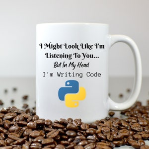 May include: White ceramic mug with the text "I Might Look Like I'm Listening To You... But In My Head I'm Writing Code" and a blue and yellow Python logo. The mug is surrounded by coffee beans.