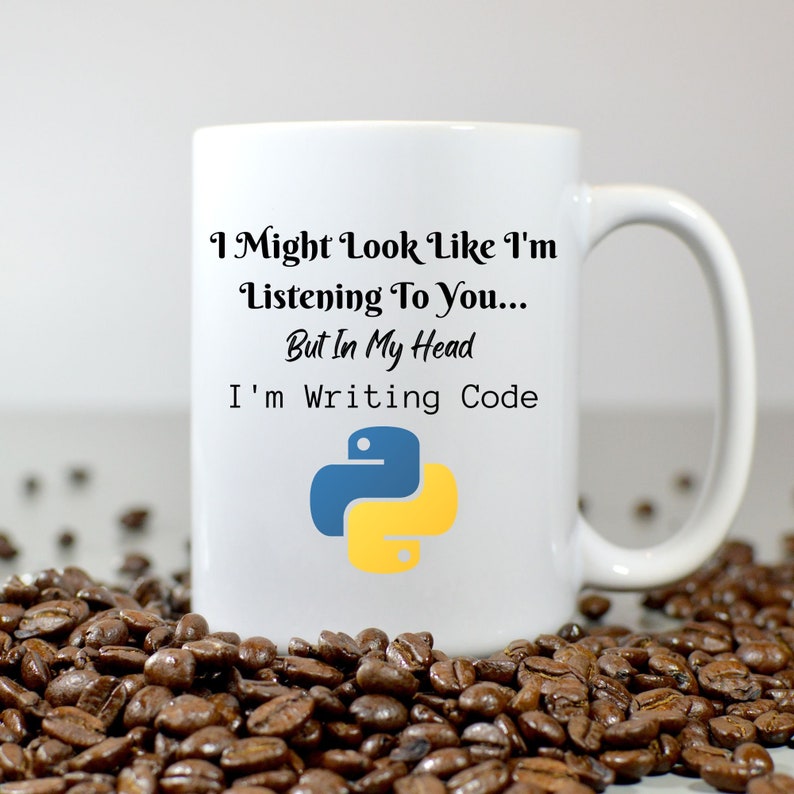 K&ouml;nnte beinhalten: Wei&szlig;e Keramik-Tasse mit dem Text "I Might Look Like I'm Listening To You... But In My Head I'm Writing Code" und einem blau-gelben Python-Logo. Die Tasse ist von Kaffeebohnen umgeben.