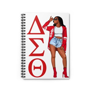 May include: A white notebook with a red, white and blue design. The notebook features a woman wearing a red jacket with the letters "ΔΣΘ" on it. The notebook has a spiral binding.