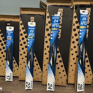 May include: A selection of new windshield wiper blades in their packaging, sizes 17, 22, 24, and 28 inches (43, 56, 61, and 71 cm). The packaging is blue and white with "ECOGARD" and "APEX" printed. Brown boxes are in the background.