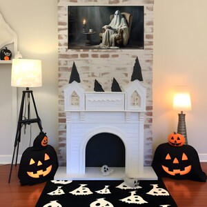 May include: A white faux fireplace with a black interior, decorated for Halloween with black fabric pumpkins and a black and white ghost rug. The fireplace is set against a brick wall with a painting of a ghost sitting in a chair.
