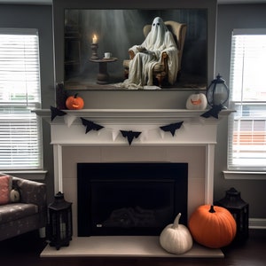 May include: A white fireplace mantel with a black fireplace and a white ghost sitting in a chair in front of a fireplace. The ghost is holding a book and there are pumpkins and bats on the mantel.