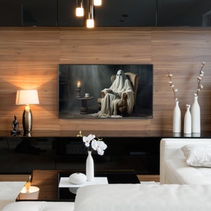 May include: A white ghost figure sits in a chair, reading a book, in a dimly lit room. A candle and a cup are on a small table next to the chair. The image is framed and hanging on a wall in a modern living room.