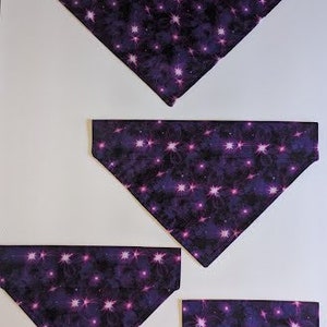 May include: Four purple dog bandanas with a pink and purple star pattern. The bandanas are arranged in a pyramid shape, with the largest bandana at the top and the smallest bandana at the bottom.