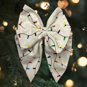 Könnte beinhalten: Eine weiße Schleife aus Stoff mit einem Muster aus bunten Weihnachtslichtern. Die Schleife ist eine festliche Dekoration für einen Weihnachtsbaum oder ein Geschenk.