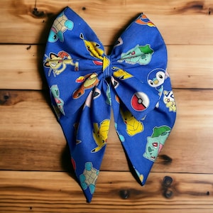 May include: A blue fabric bow with a Pokemon character print. The bow features characters like Squirtle, Bulbasaur, and Pikachu.