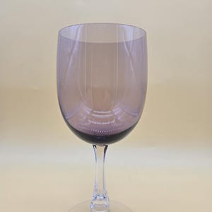 May include: A wine glass featuring a translucent, deep purple-tinted bowl that transitions into a clear, slender stem and a wide, circular base. The glass has a smooth, rounded rim and a polished finish, showcasing a simple, elegant design.