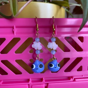 May include: A pair of gold dangle earrings with blue raindrop charms and white cloud beads.
