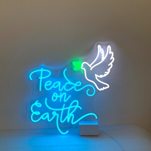 May include: A neon sign with a white dove holding an olive branch in its beak. The sign says "Peace on Earth" in a blue neon font.