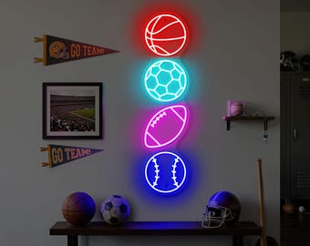 May include: A wall-mounted display featuring four neon sports ball lights: a red basketball, a turquoise soccer ball, a magenta football, and a blue baseball. The wall also has pennants that say "GO TEAM!" and a framed stadium photo.