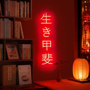 May include: A vertical neon sign emitting a bright red glow, featuring the Japanese kanji characters 生き甲斐, which translates to ikigai. The sign is mounted on a wall, casting a warm red light across the surrounding space and nearby objects.