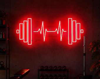 Op de afbeelding: Een rood neonbord in de vorm van een halter met een hartslaglijn in het midden. Het bord is bevestigd aan een donkere muur in een sportschool. Andere fitnessapparatuur is zichtbaar op de achtergrond, waaronder gewichten en een bank.