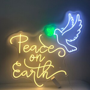 May include: A neon sign with a white dove carrying a green olive branch. The sign reads "Peace on Earth" in yellow neon.