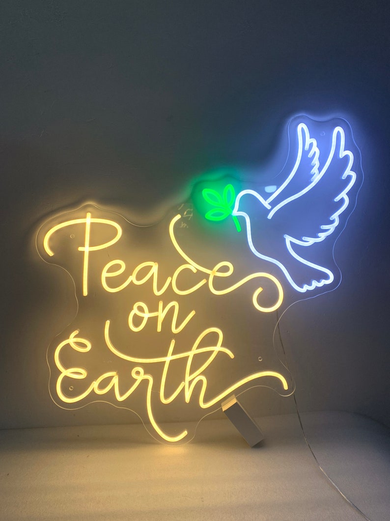 May include: A neon sign with a white dove carrying a green olive branch. The sign reads "Peace on Earth" in yellow neon.