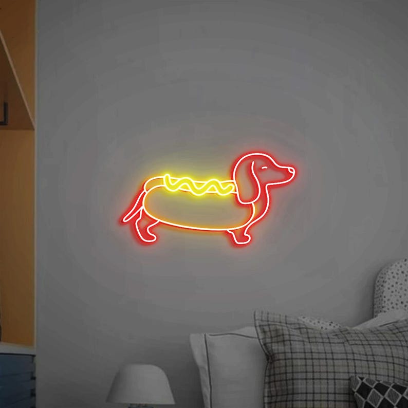 Op de afbeelding: Een neonbord in de vorm van een teckel die een hotdogkostuum draagt. De hond is rood en de hotdog is geel met mosterd.