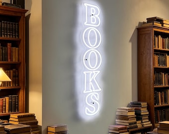May include: A white neon sign spelling "BOOKS" is mounted on a light gray wall. The sign is surrounded by wooden bookshelves filled with books. Stacks of books are also placed on the floor in front of the shelves, creating a cozy library atmosphere.