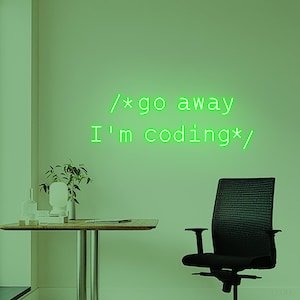 以下が含まれることがあります： 壁に緑色のネオンサインがあり、「/*go away I'm coding*/」と書かれています。 部屋には机、黒いオフィスチェア、小さな植物があります。 全体的なカラースキームは緑色です。
