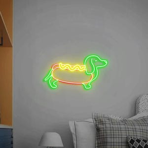 Op de afbeelding: Een neonbord in de vorm van een teckel die een hotdogkostuum draagt. De hond is groen, de hotdog is geel en de mosterd is geel.