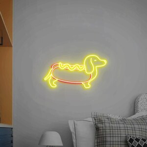 Op de afbeelding: Een geel neonbord in de vorm van een teckel met een hotdog erin. De hotdog heeft een gele mosterdlijn bovenop.