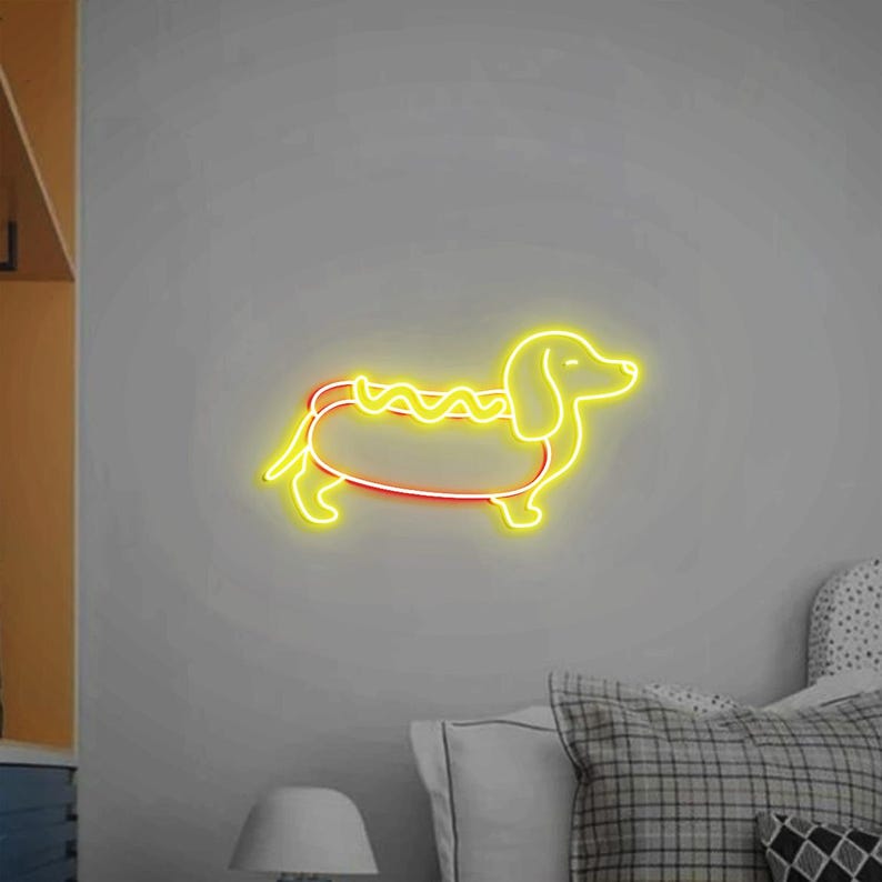 Op de afbeelding: Een geel neonbord in de vorm van een teckel met een hotdog erin. De hotdog heeft een gele mosterdlijn bovenop.