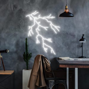 May include: A white neon lightning bolt wall art. The lightning bolt is mounted on a grey textured wall. A black desk lamp, a black pendant light, and a telescope are also visible. A brown coat hangs on a black chair.