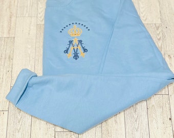 May include: A light blue sweatshirt with a gold embroidered crown and initials. The initials are "M.V." and are surrounded by a circle of stars.