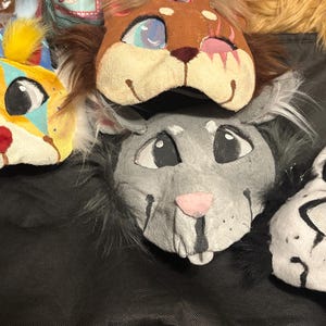 Op de afbeelding: Vier dierenmaskers met gestileerde ontwerpen. E&eacute;n masker is geel met blauwe accenten en geel bont, &eacute;&eacute;n is bruin met donker bont, &eacute;&eacute;n is grijs met donker bont en &eacute;&eacute;n is wit met zwarte markeringen. Elk masker heeft gaas over de ogen.